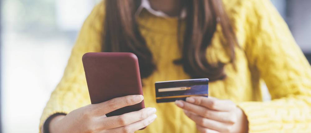 Eine Frau hält ein Smartphone in der einen und die Kreditkarte in der anderen Hand.