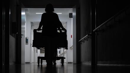 Eine Pflegerin schiebt ein Krankenbett durch den Gang einer Klinikstation.