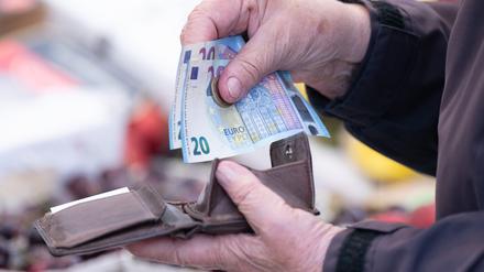 Eine Frau sortiert auf einem Wochenmarkt das Wechselgeld für ihre Einkäufe in ein Portemonnaie. 