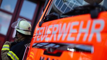 Eine Einsatzkraft der Feuerwehr steht neben einem Einsatzfahrzeug der Feuerwehr. 