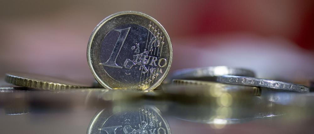 Eine 1-Euro-Münze steht auf einem Tisch, umgeben von anderen Euro-Münzen. 