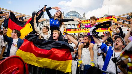 Deutschland-Fans feiern beim Public Viewing in der Fanzone am Reichstagsgebäude mit schwarz-rot-goldenen Schals und Flaggen.