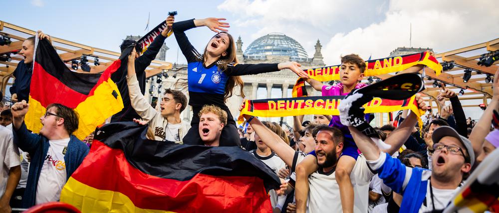 Deutschland-Fans feiern beim Public Viewing in der Fanzone am Reichstagsgebäude mit schwarz-rot-goldenen Schals und Flaggen.