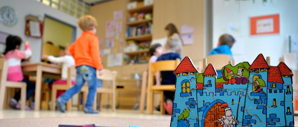 Kleinkinder spielen zusammen in einer Kita. Bauklötze und ein Spielzeugschloss stehen in dem Raum.