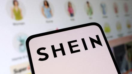 Ein Smartphone, auf dem das Shein-Logo zu sehen ist, wird vor einen Monitor mit der Shein-Website gehalten.