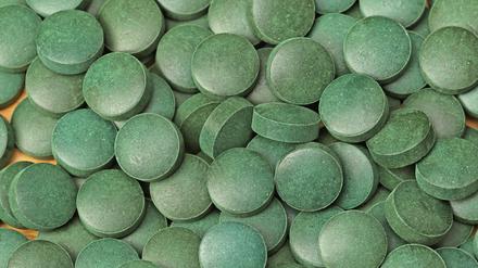 Ein Haufen kleiner grüner Tabletten aus gepresstem Spirulina-Pulver.
