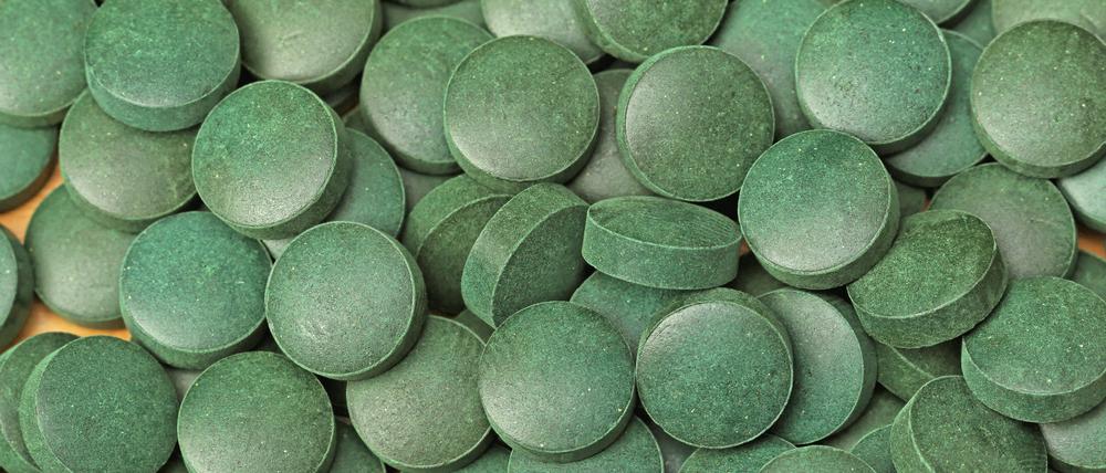Ein Haufen kleiner grüner Tabletten aus gepresstem Spirulina-Pulver.