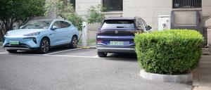 Ein chinesisches E-Auto des Herstellers Denza (l) steht neben einem deutschen E-Auto ID.6 von Volkswagen an einer Ladestation.