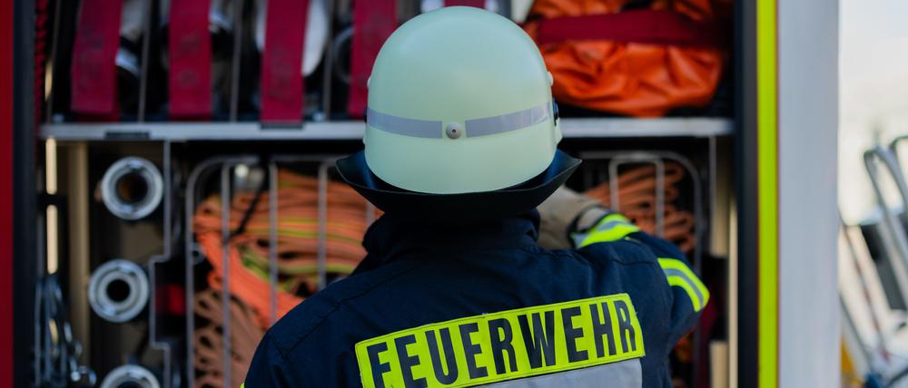 Ein Feuerwehrmann steht am Feuerwehrauto und sucht einen Schlauch raus. 