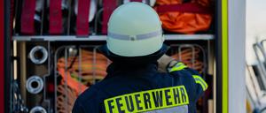 Ein Feuerwehrmann steht am Feuerwehrauto und sucht einen Schlauch raus. 