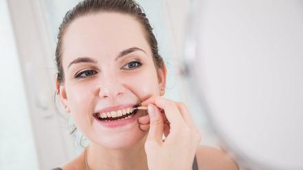 Eine Frau reinigt mit einer Interdentalbürste die Zwischenräume ihrer Zähne.