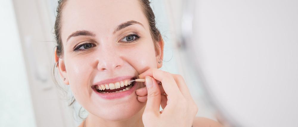 Eine Frau reinigt mit einer Interdentalbürste die Zwischenräume ihrer Zähne.