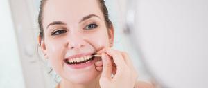 Eine Frau reinigt mit einer Interdentalbürste die Zwischenräume ihrer Zähne.
