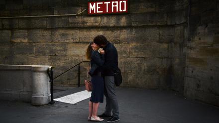 Ein Pärchen küsst sich vor einem Eingang der Pariser Metro.