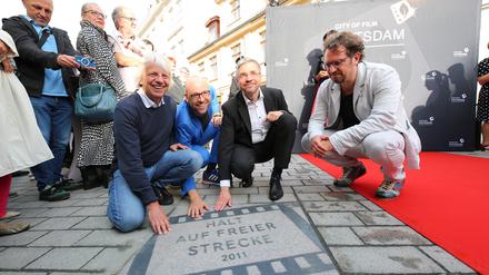 Regisseur Andreas Dresen, der Schauspieler und Autor Sebastian Stielke, Potsdams Oberbürgermeister Mike Schubert und der Filmwissenschaftler Chris Wahl hocken vor einer Platte mit dem Titel „Halt auf freier Strecke“ bei der Eröffnung des „Boulevard des Films“ (von links).
