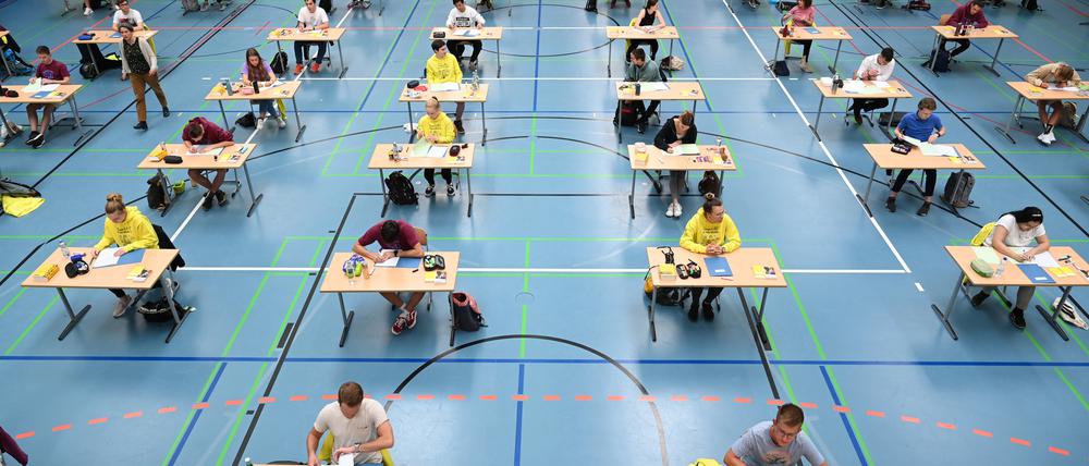 Schülerinnen sitzen während der Deutsch-Abitursprüfung mit dem vorgeschriebenen Abstand zueinander in einer Sporthalle.