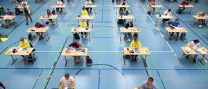 Schülerinnen sitzen während der Deutsch-Abitursprüfung mit dem vorgeschriebenen Abstand zueinander in einer Sporthalle. 