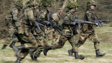 Mit Blattwerk und Gras getarnte Wehrpflichtige von den Panzergrenadieren rennen mit ihren Waffen im Rahmen ihrer Grundausbildung bei einer Übung. 