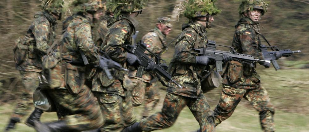 Mit Blattwerk und Gras getarnte Wehrpflichtige von den Panzergrenadieren rennen mit ihren Waffen im Rahmen ihrer Grundausbildung bei einer Übung. 
