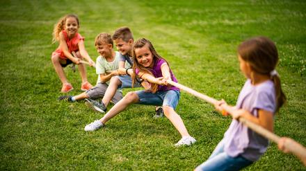 Kinder spielen Tauziehen in grüner Natur.