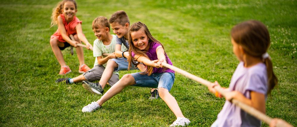 Kinder spielen Tauziehen in grüner Natur.