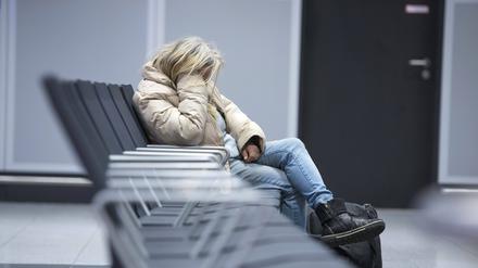 Eine Obdachlose sitzt in gekrümmter Haltung auf einer Bank.