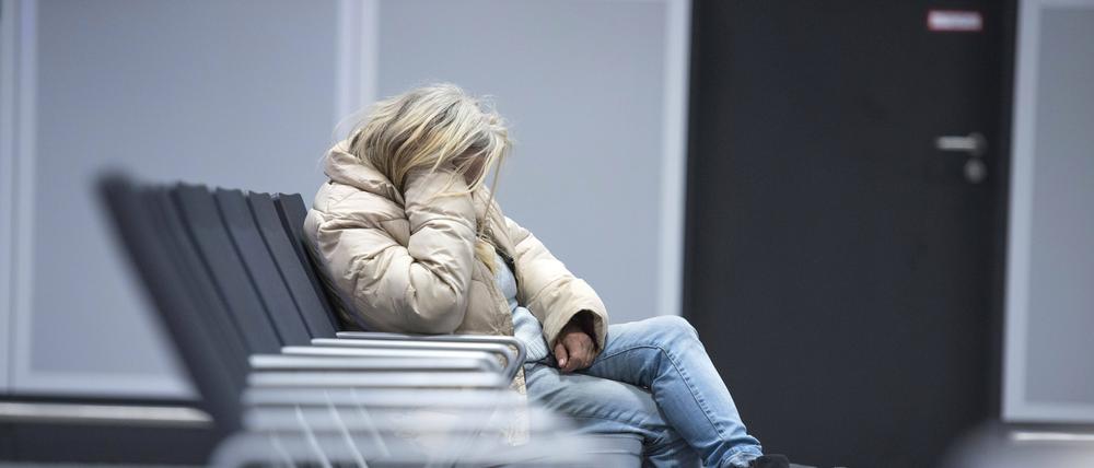 Eine Obdachlose sitzt in gekrümmter Haltung auf einer Bank.