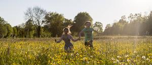 Zwei Kinder laufen über ein Feld voller blühender Blumen.