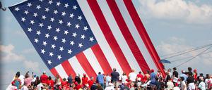 Anhänger von Donald Trump vor einer riesigen US-Flagge bei einer Wahlkampfveranstaltung.