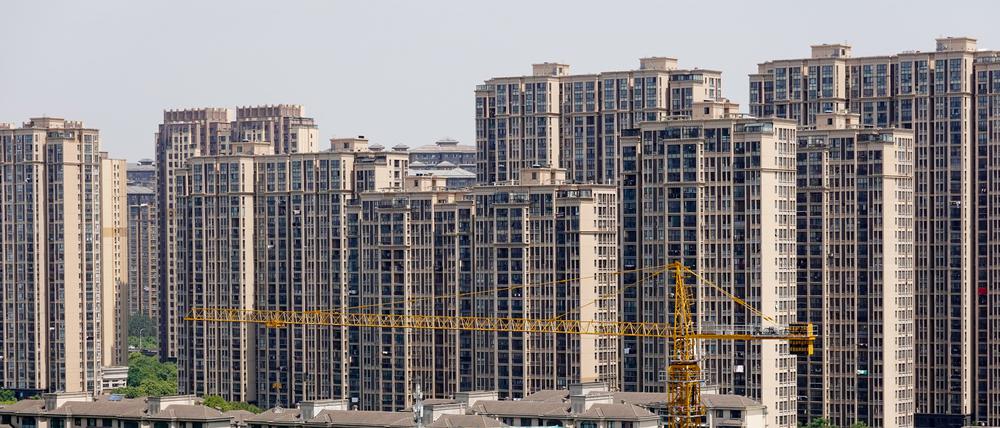 China, Changzhou: Ein Baukran steht neben einem im Bau befindlichen Gebäude vor fertig gestellten Wohnhäusern. Die anhaltende Immobilienkrise treibt die chinesische Mittelschicht um und sorgt für wirtschaftliche Ungewissheit in der Volksrepublik.