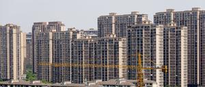 China, Changzhou: Ein Baukran steht neben einem im Bau befindlichen Gebäude vor fertig gestellten Wohnhäusern. Die anhaltende Immobilienkrise treibt die chinesische Mittelschicht um und sorgt für wirtschaftliche Ungewissheit in der Volksrepublik.