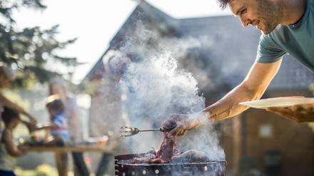 Ein Mann steht vor einem qualmenden Grill, um das Fleisch zu wenden.