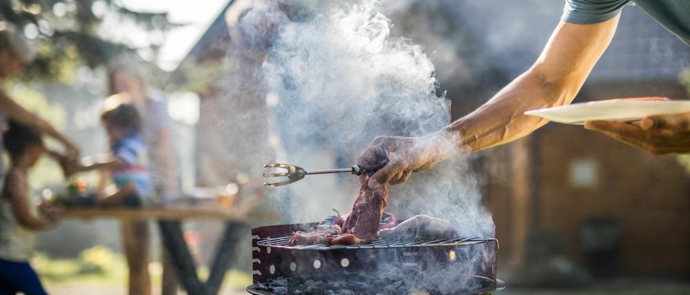 Ein Mann steht vor einem qualmenden Grill, um das Fleisch zu wenden.