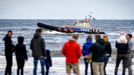 Menschen stehen in den Niederlanden am Strand von Scheveningen, ein Boot mit Einsatzkräften fährt vorbei. An einer anderen Stelle an der Nordsee, in Bergen aan Zee, ist ein deutscher Tourist in der Nordsee ertrunken.