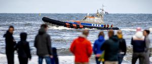 Menschen stehen in den Niederlanden am Strand von Scheveningen, ein Boot mit Einsatzkräften fährt vorbei. An einer anderen Stelle an der Nordsee, in Bergen aan Zee, ist ein deutscher Tourist in der Nordsee ertrunken.