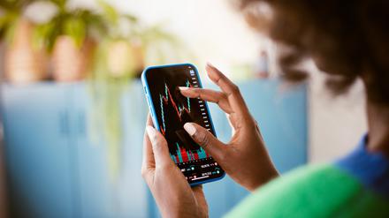 Eine junge Frau beobachtet ihren Aktienkurs auf dem Handy.