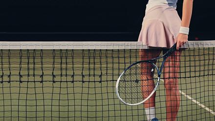 Eine Tennisspielerin lehnt sich suggestiv mit ihrem rosa Minirock an ein Tennisnetz.