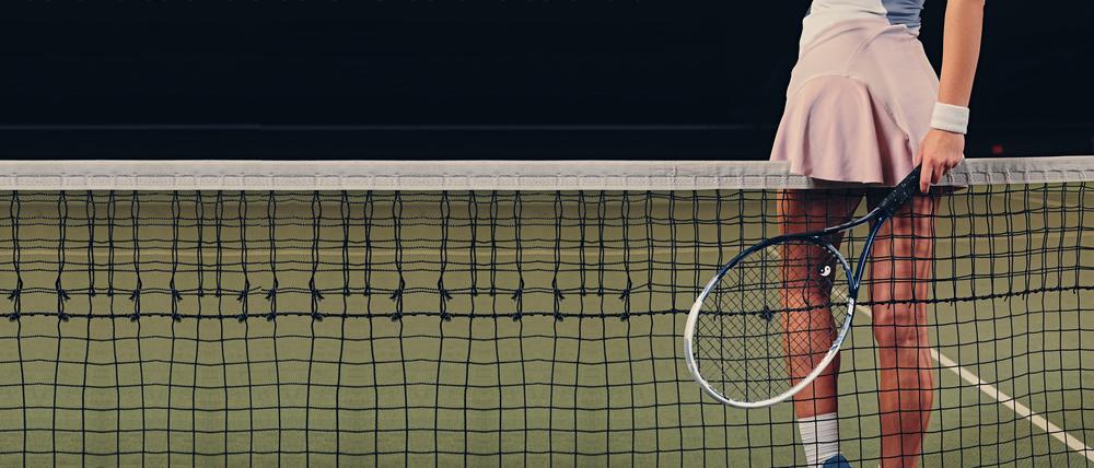 Eine Tennisspielerin lehnt sich suggestiv mit ihrem rosa Minirock an ein Tennisnetz.