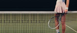 Eine Tennisspielerin lehnt sich suggestiv mit ihrem rosa Minirock an ein Tennisnetz.