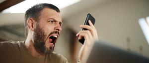 Frustrierter Mann, der jemanden durch einen Anruf über sein Smartphone zu Hause anschreit.