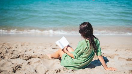 Eine Frau liest ein Buch am Strand.
