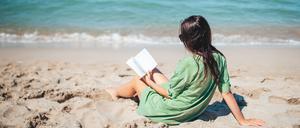 Eine Frau liest ein Buch am Strand.