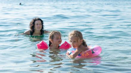 The sisters swim in the sea. The mother swims next to the children. Children use inflatable armlets and an inflatable ring for safety.