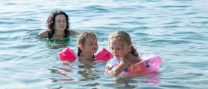 The sisters swim in the sea. The mother swims next to the children. Children use inflatable armlets and an inflatable ring for safety.