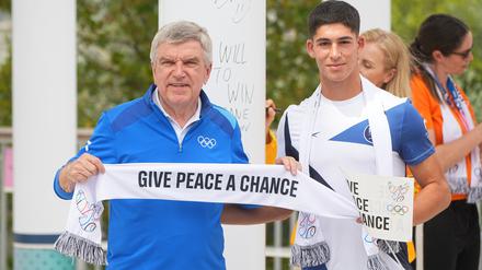 IOC-Präsident Thomas Bach hält während einer Veranstaltung, bei der das Wandbild des Olympischen Friedens für Paris 2024, eingeweiht wird, mit dem Fußballer Niv Yehoshua aus Israel einen Schal mit der Aufschrift „give peace a chance“ in Händen. 