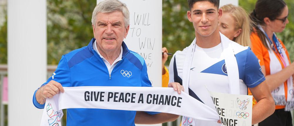 IOC-Präsident Thomas Bach hält während einer Veranstaltung, bei der das Wandbild des Olympischen Friedens für Paris 2024, eingeweiht wird, mit dem Fußballer Niv Yehoshua aus Israel einen Schal mit der Aufschrift „give peace a chance“ in Händen. 