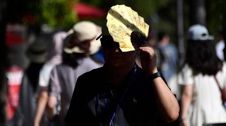 Ein Tourist nutzt einen Fächer, um sich vor der Sonne zu schützen, als er am 23. Juli 2024 auf einer Straße in Sevilla spaziert. 