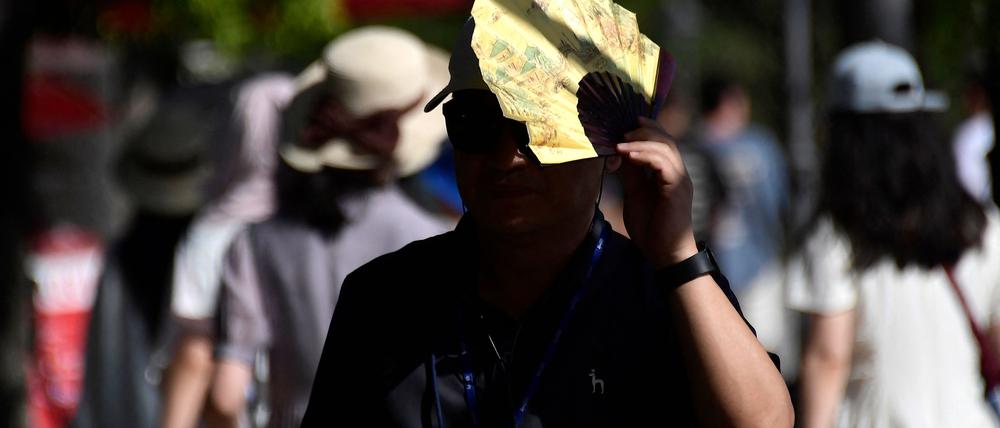 Ein Tourist nutzt einen Fächer, um sich vor der Sonne zu schützen, als er am 23. Juli 2024 auf einer Straße in Sevilla spaziert.