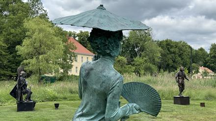 Eine Bronzeskulptur von einer barock gekleideten Frau mit Sonnenschirm und Fächer im Skulpturengarten im Schlossgut Schwante.