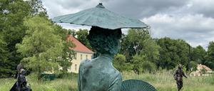 Eine Bronzeskulptur von einer barock gekleideten Frau mit Sonnenschirm und Fächer im Skulpturengarten im Schlossgut Schwante.